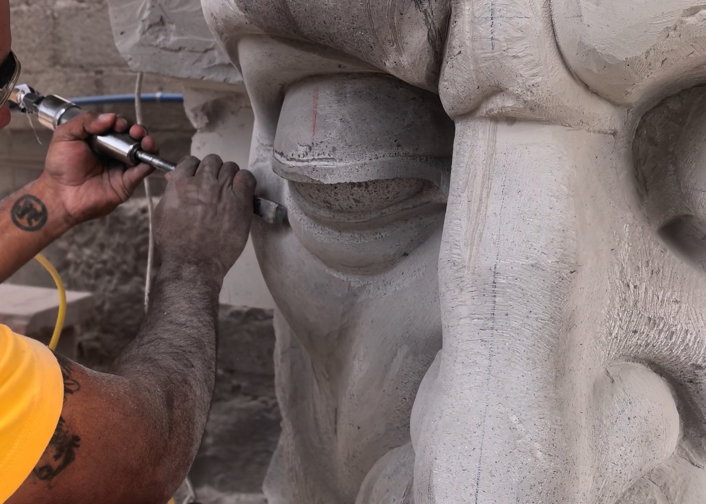 Escultor rematando a mano con cincel neumático el rostro de una escultura monumental de cantera