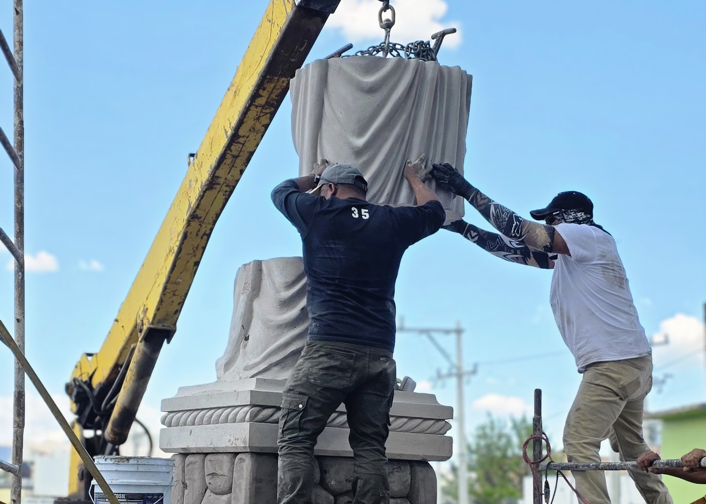 Instalación en sitio: dos operarios colocan con grúa una escultura de cantera sobre su base